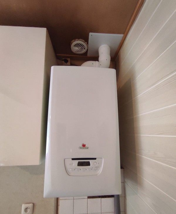 Chaudière murale blanche avec affichage numérique, tuyaux et bouton de commande.