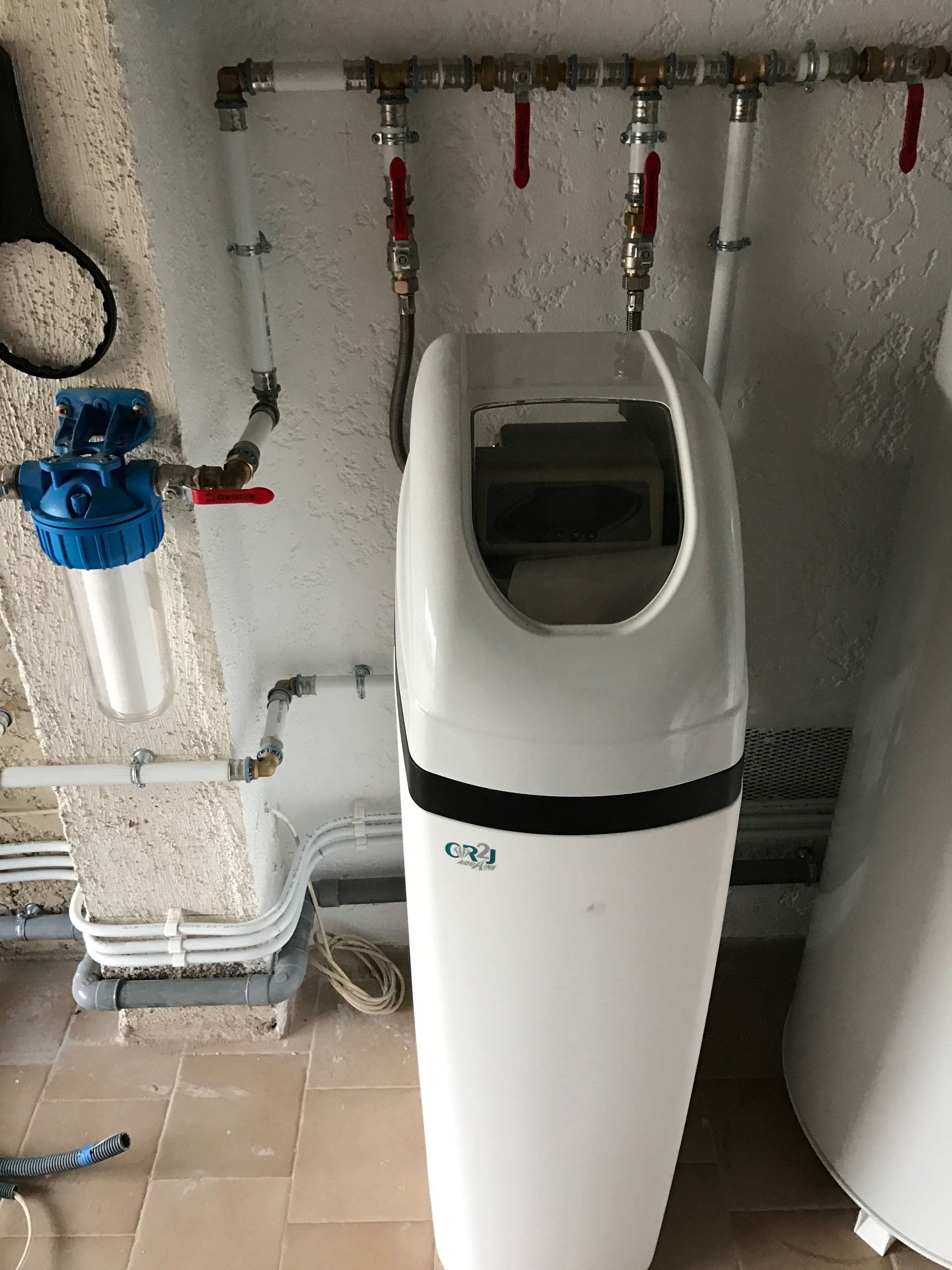 Système de filtration d'eau avec boîtiers bleus, filtres blancs et transparents, raccordé à des tuyaux blancs et rouges, monté sur un mur en briques.