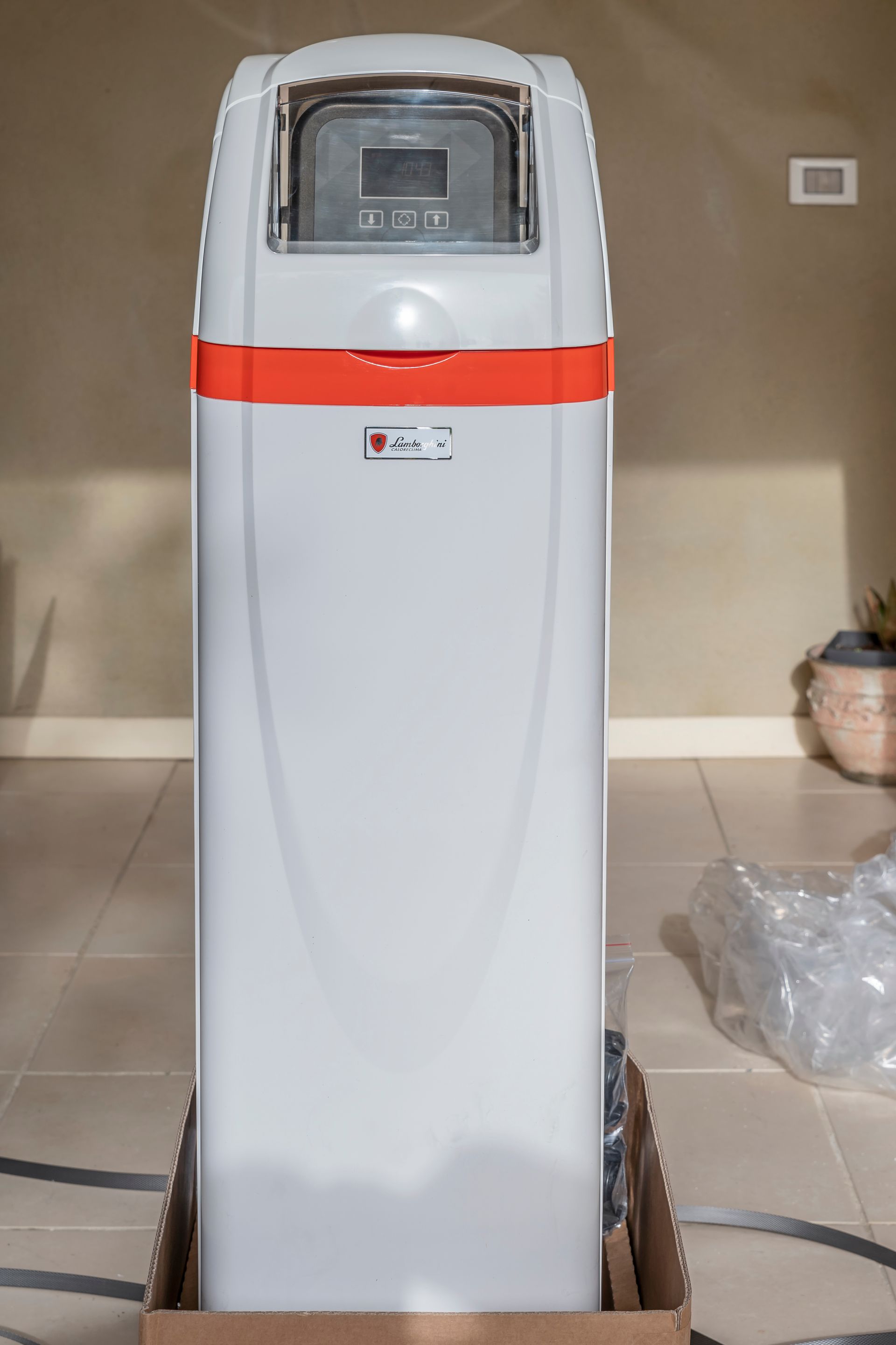 Adoucisseur d'eau blanc avec bande orange, dans une boîte en carton, à l'intérieur.