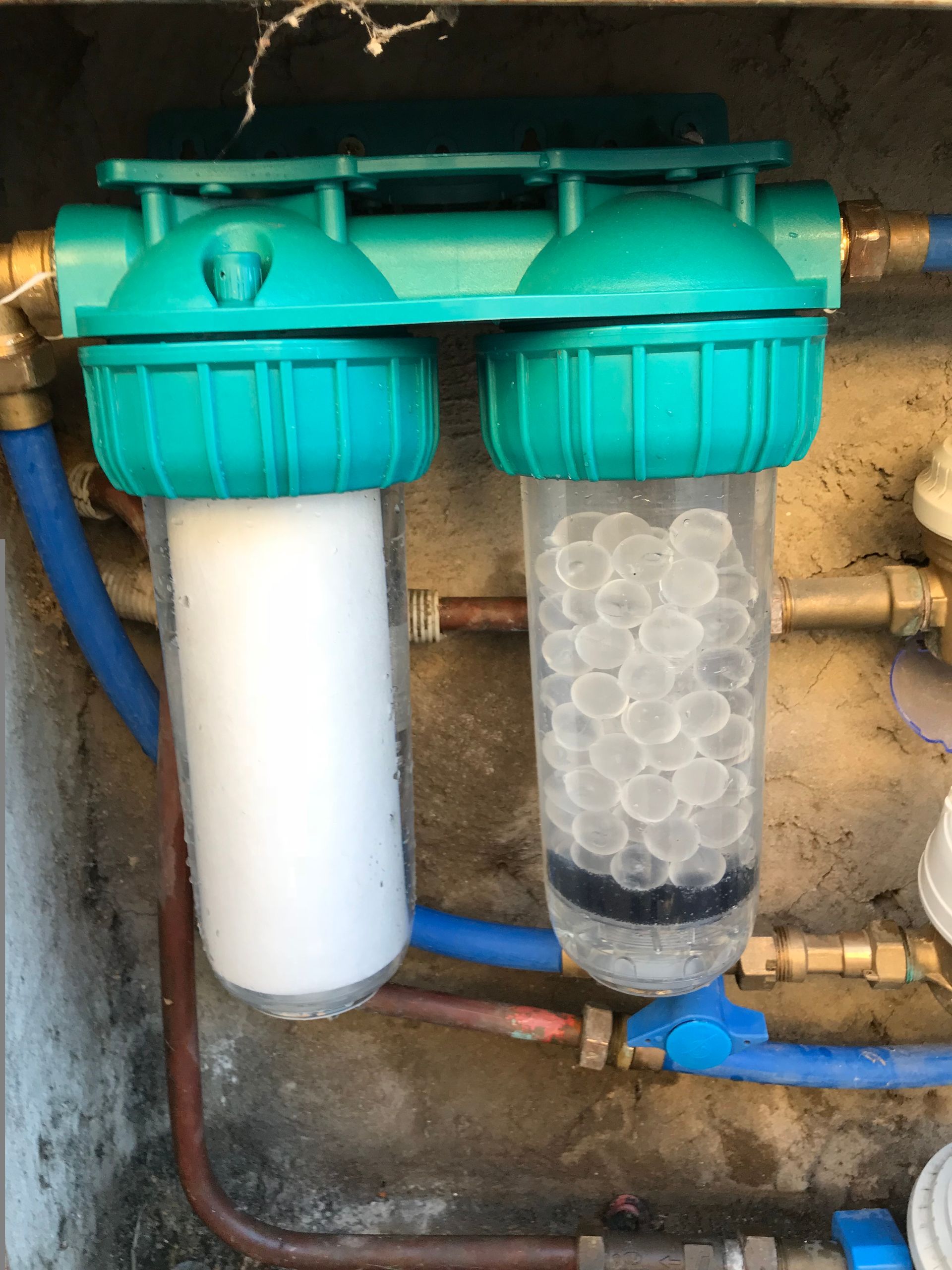 Deux filtres à eau, bouchons turquoise, un filtre blanc, un filtre transparent rempli de billes, tuyaux fixés.