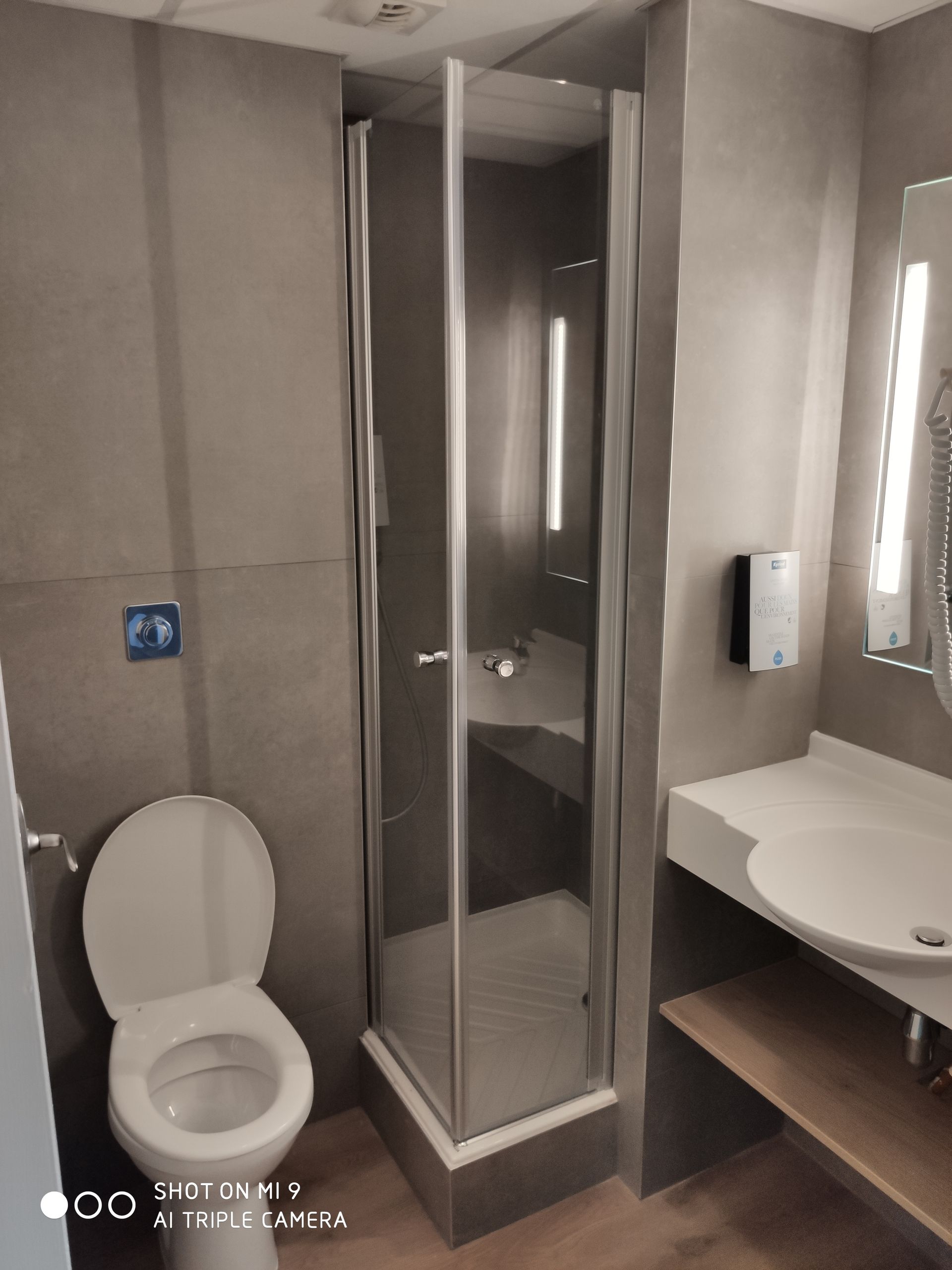 Salle de bains avec toilettes, cabine de douche et lavabo contre des murs gris.