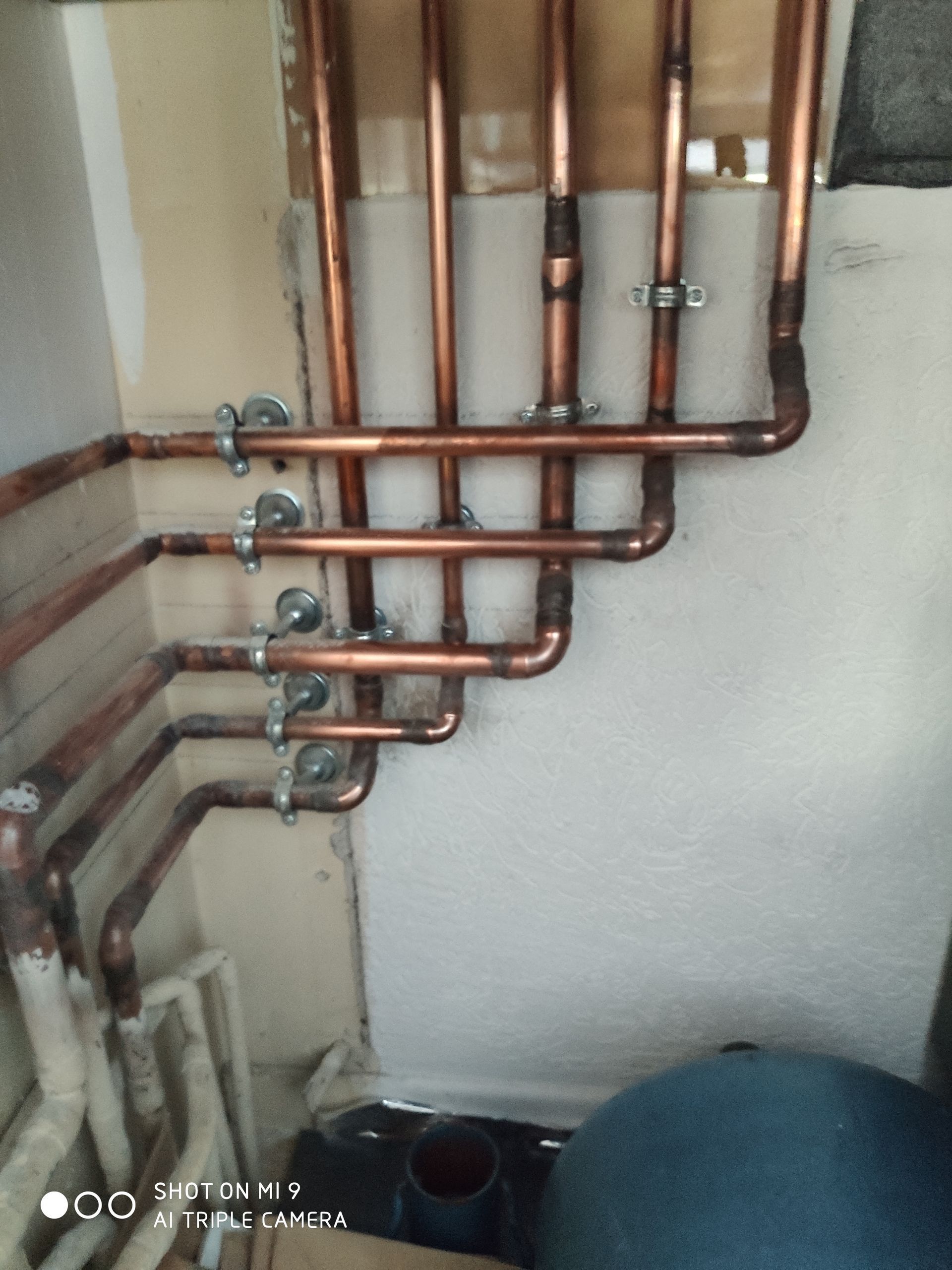 Des tuyaux en cuivre fixés à des supports blancs forment un système de chauffage ou de plomberie contre un mur clair.