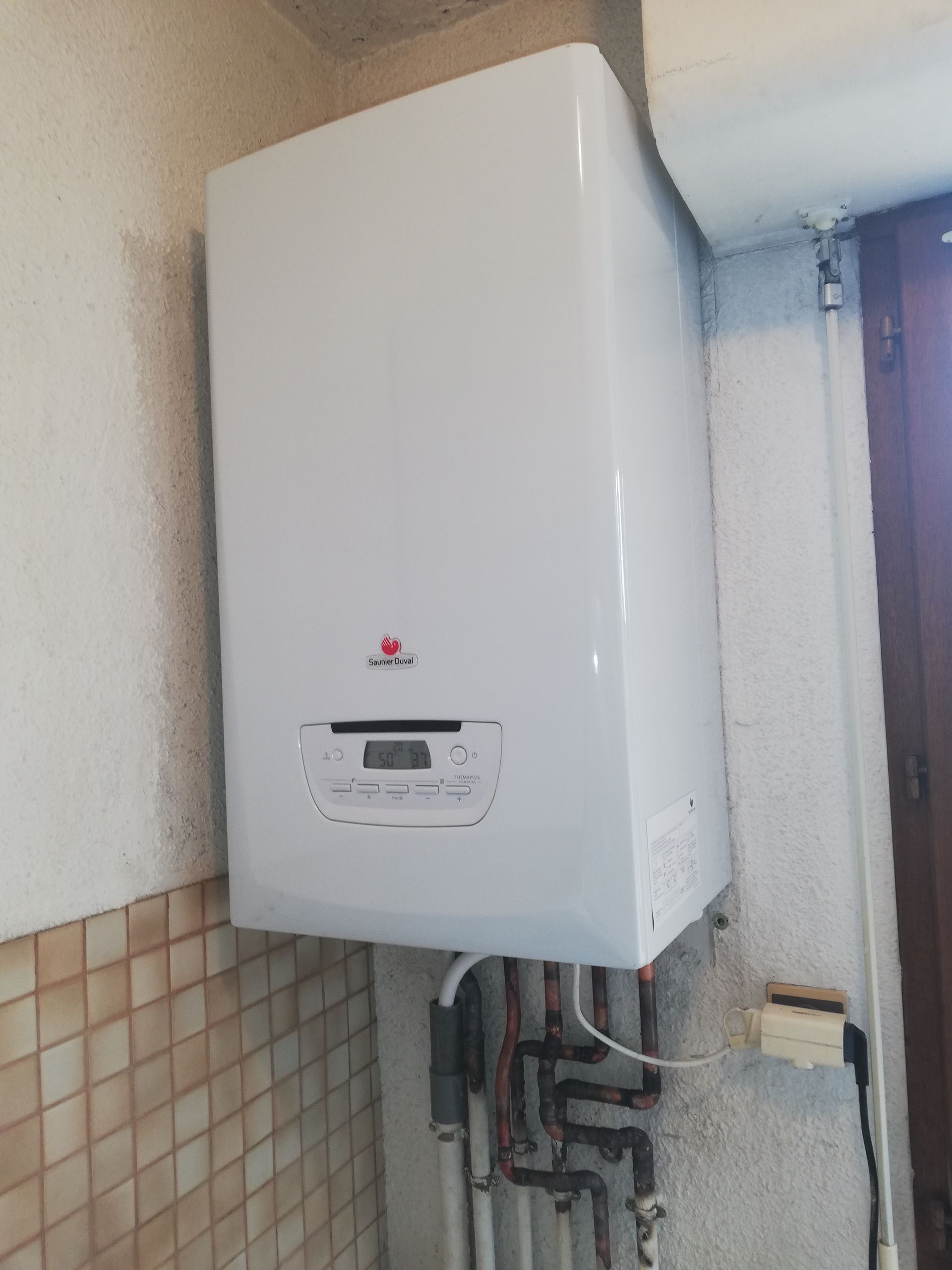 Chaudière à gaz murale blanche avec affichage numérique et logo rouge sur un mur carrelé.