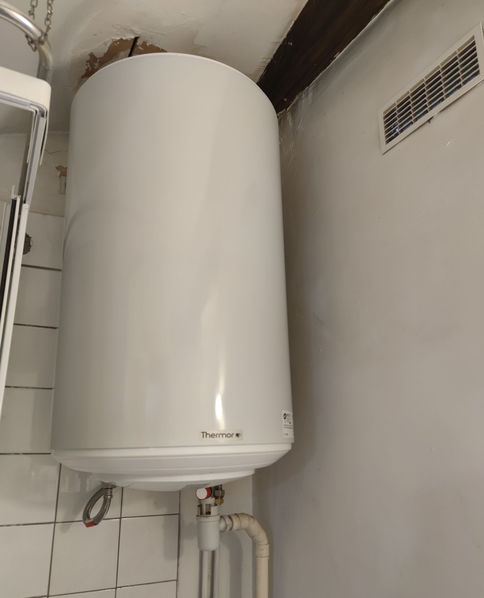 Chauffe-eau blanc fixé sur un mur bleu, avec des tuyaux rouges et bleus raccordés.