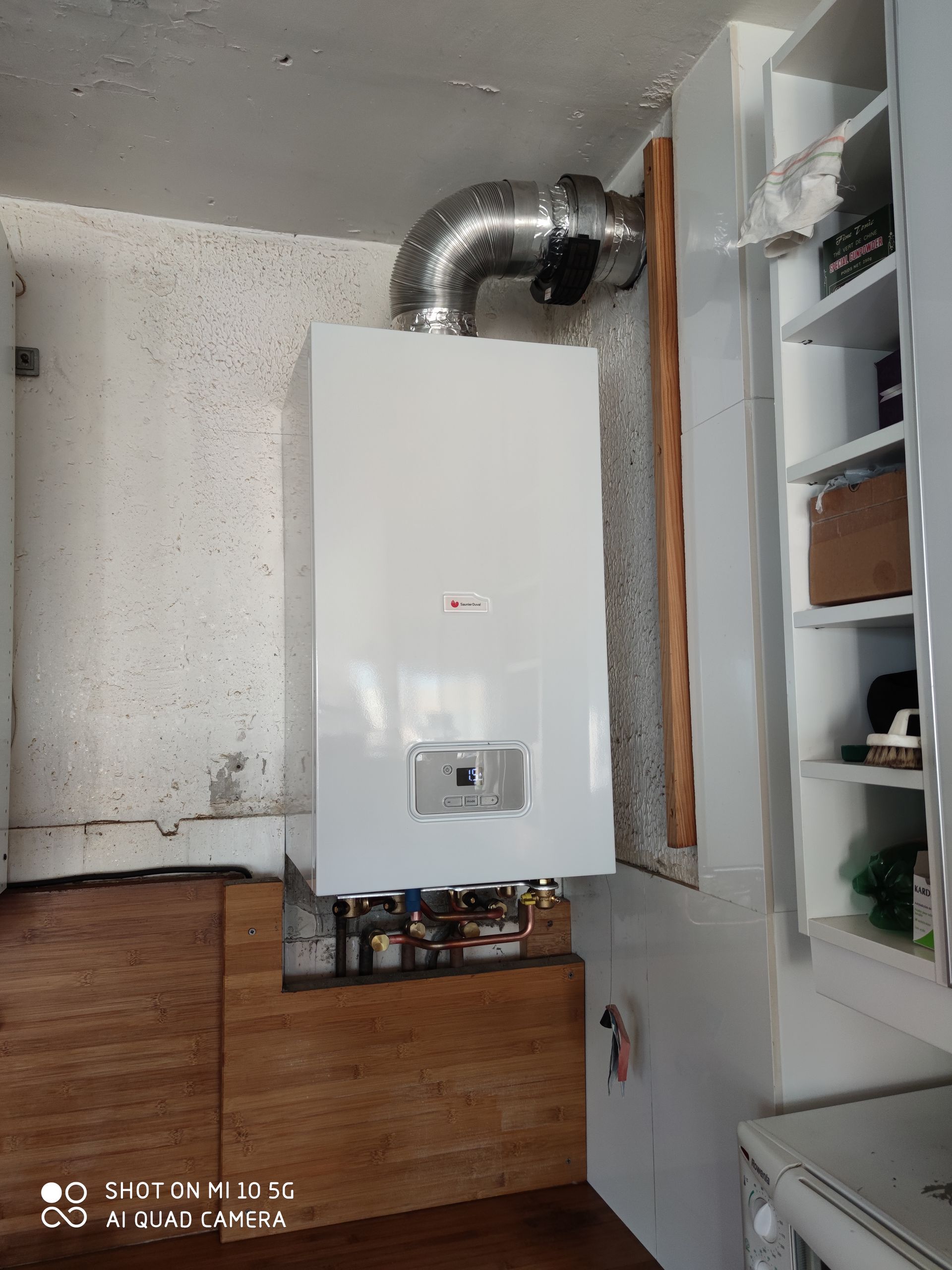 Une chaudière à gaz murale blanche avec un tuyau d'évacuation argenté, installée dans une buanderie.