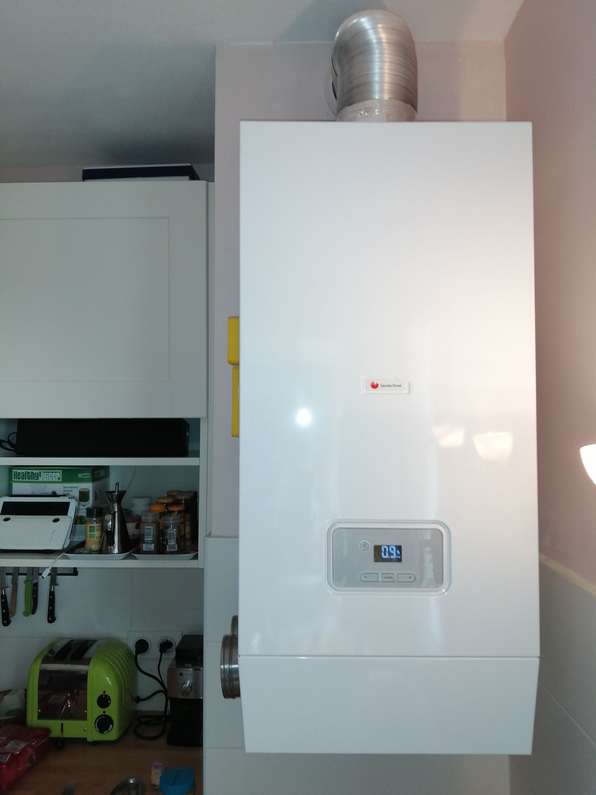 Chaudière murale blanche avec affichage numérique et tuyau d'évacuation argenté, installée dans une cuisine.