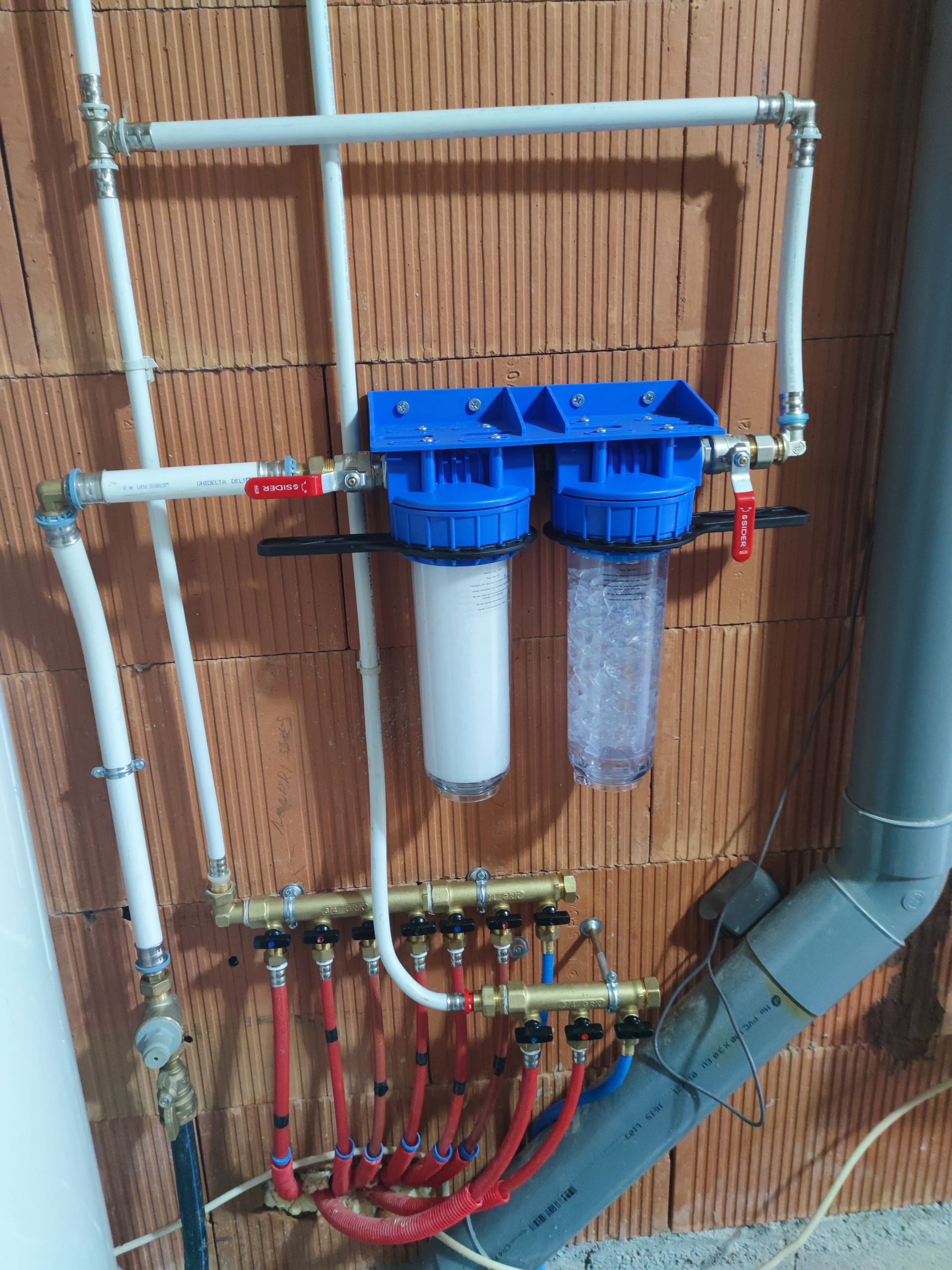 Système de filtration d'eau avec boîtiers bleus, filtres blancs et transparents, reliés à des tuyaux rouges et blancs.