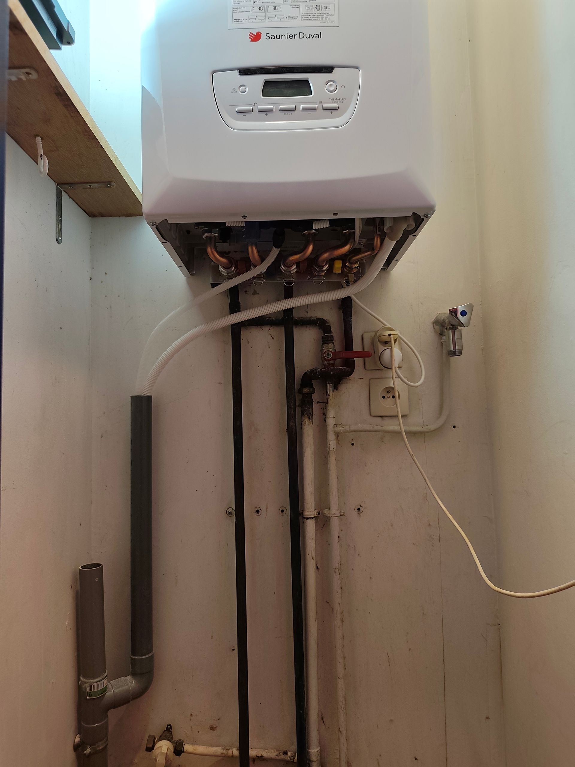 Chaudière murale blanche avec tuyauterie apparente dans une buanderie.