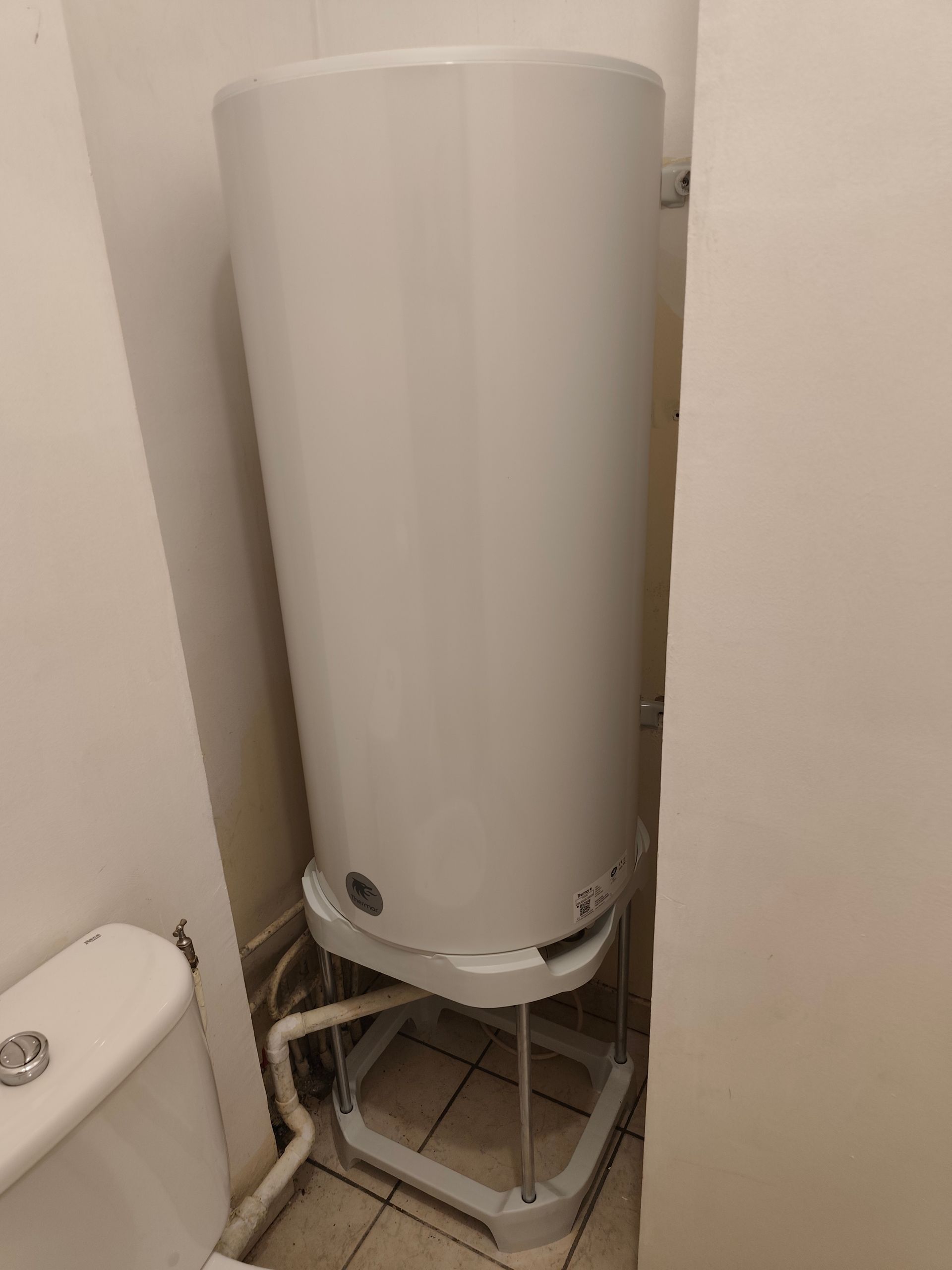 Chauffe-eau blanc dans une petite salle de bain, à côté des toilettes.