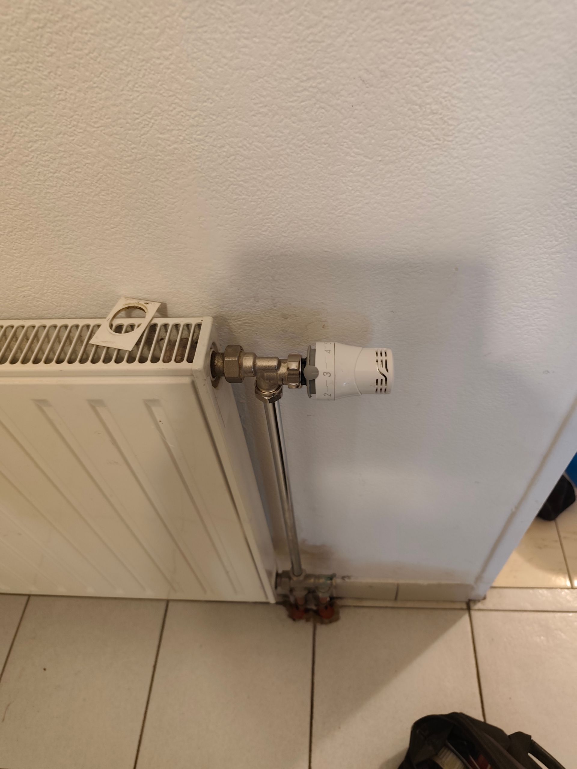 Radiateur blanc avec robinet thermostatique, fixé sur un mur blanc, à l'intérieur.