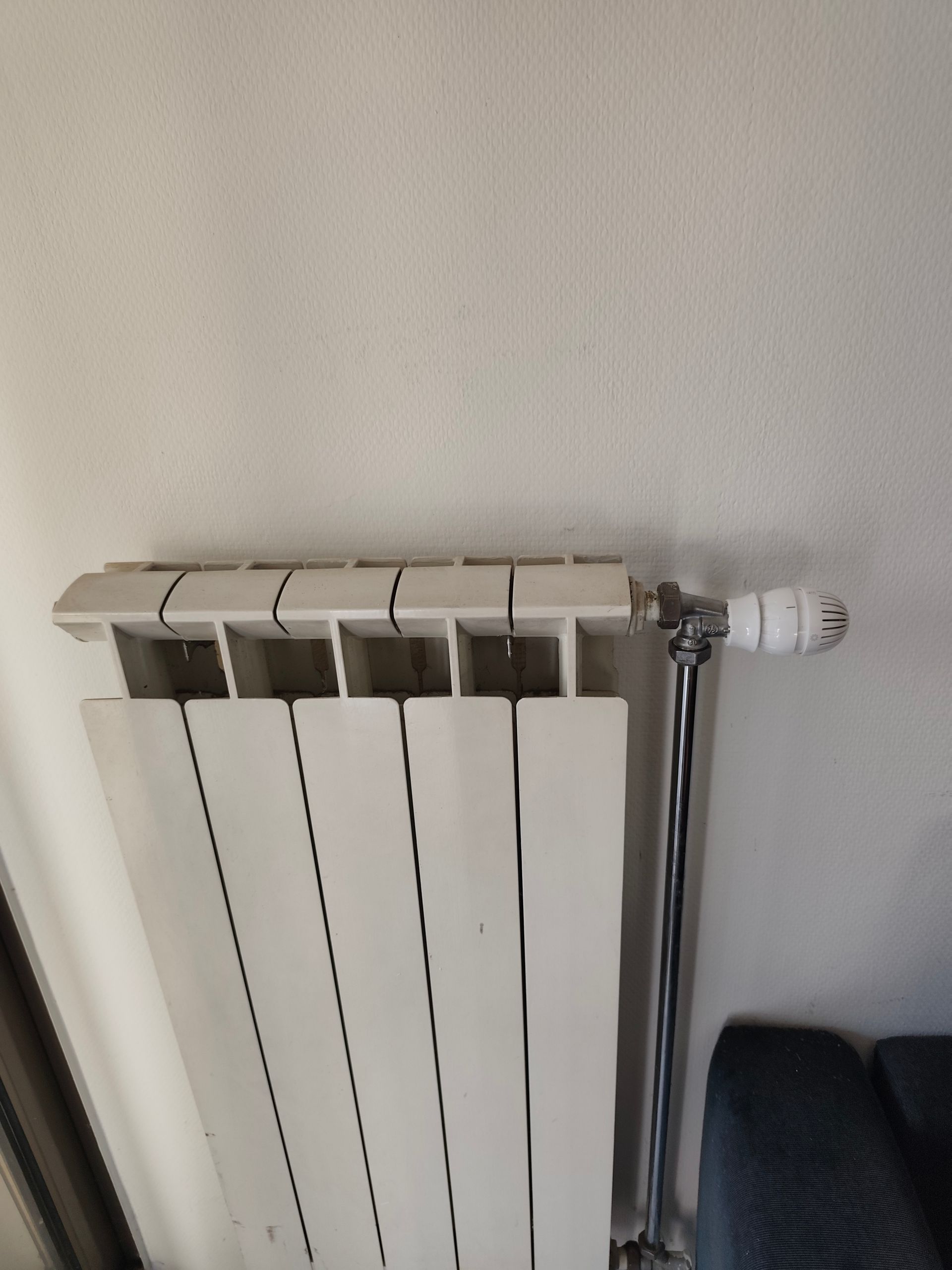 Radiateur blanc fixé sur un mur blanc, avec robinet argenté et poignée blanche.
