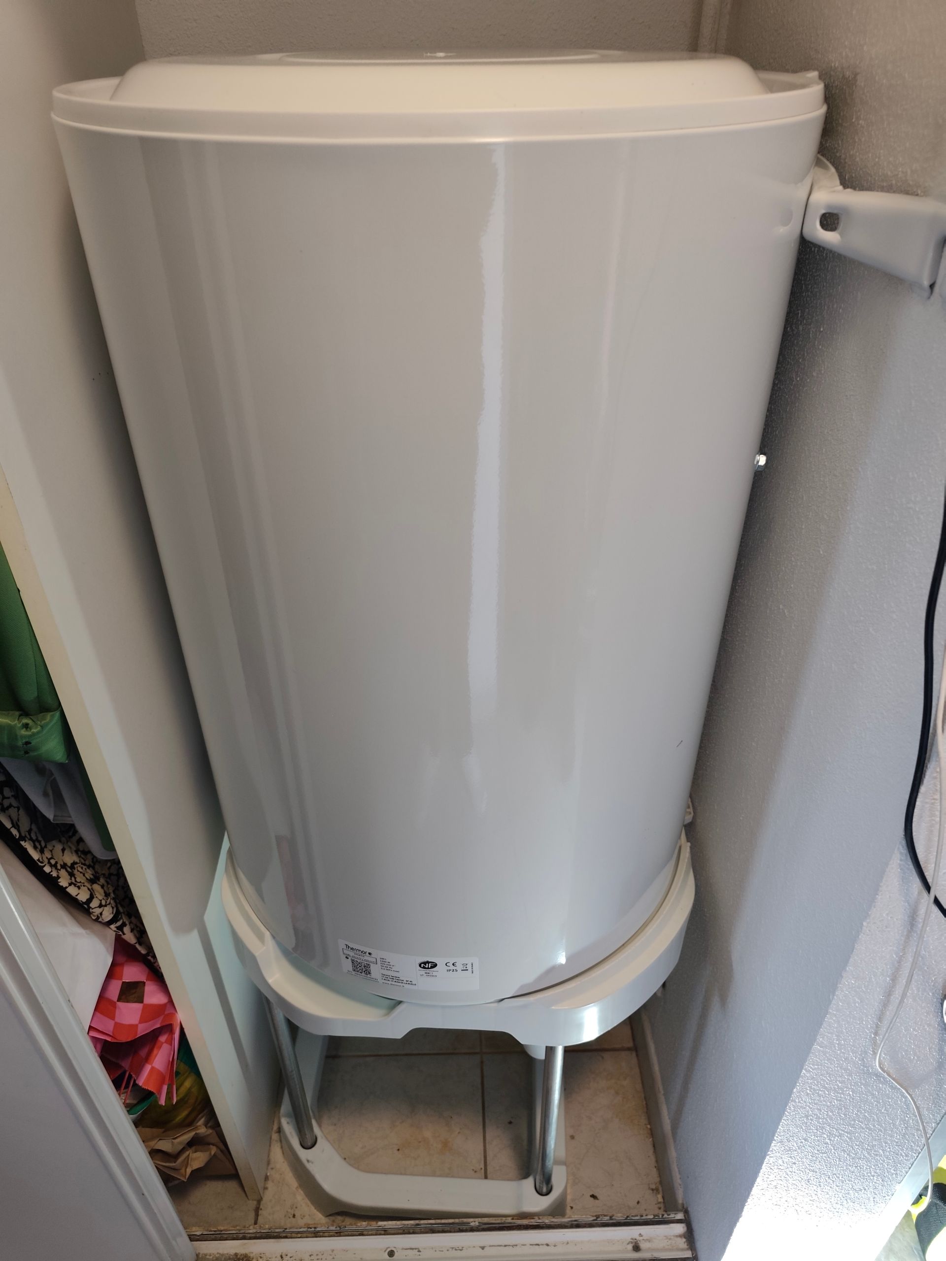 Chauffe-eau blanc installé entre les murs dans un petit espace.