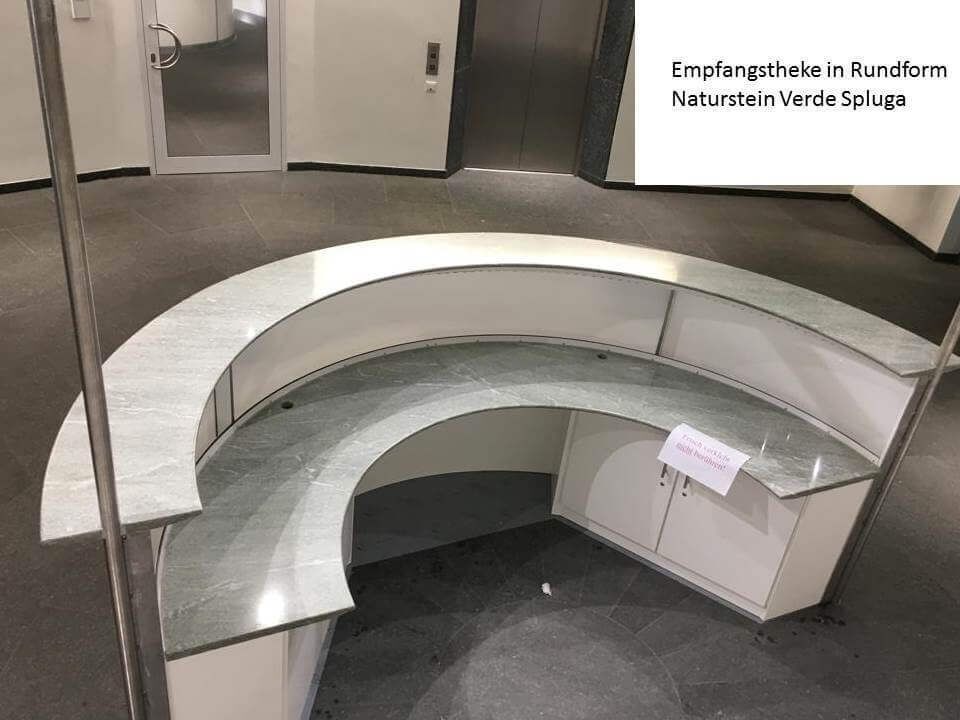 Geschwungener weißer Empfangstresen in einer modernen Bürolobby mit Teppichboden und Glastüren im hinteren Bereich