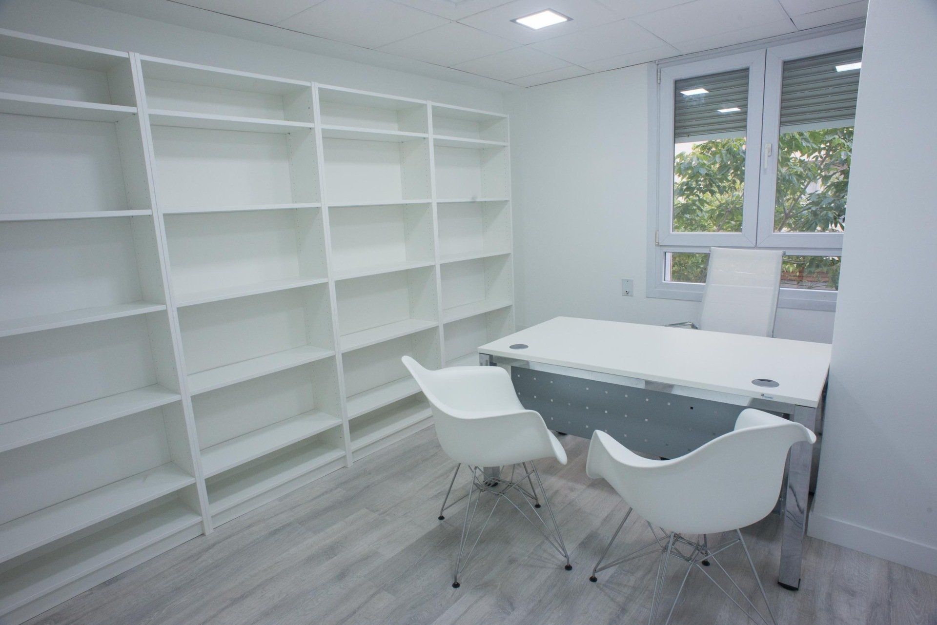 Una oficina blanca con un escritorio, sillas y estantes.