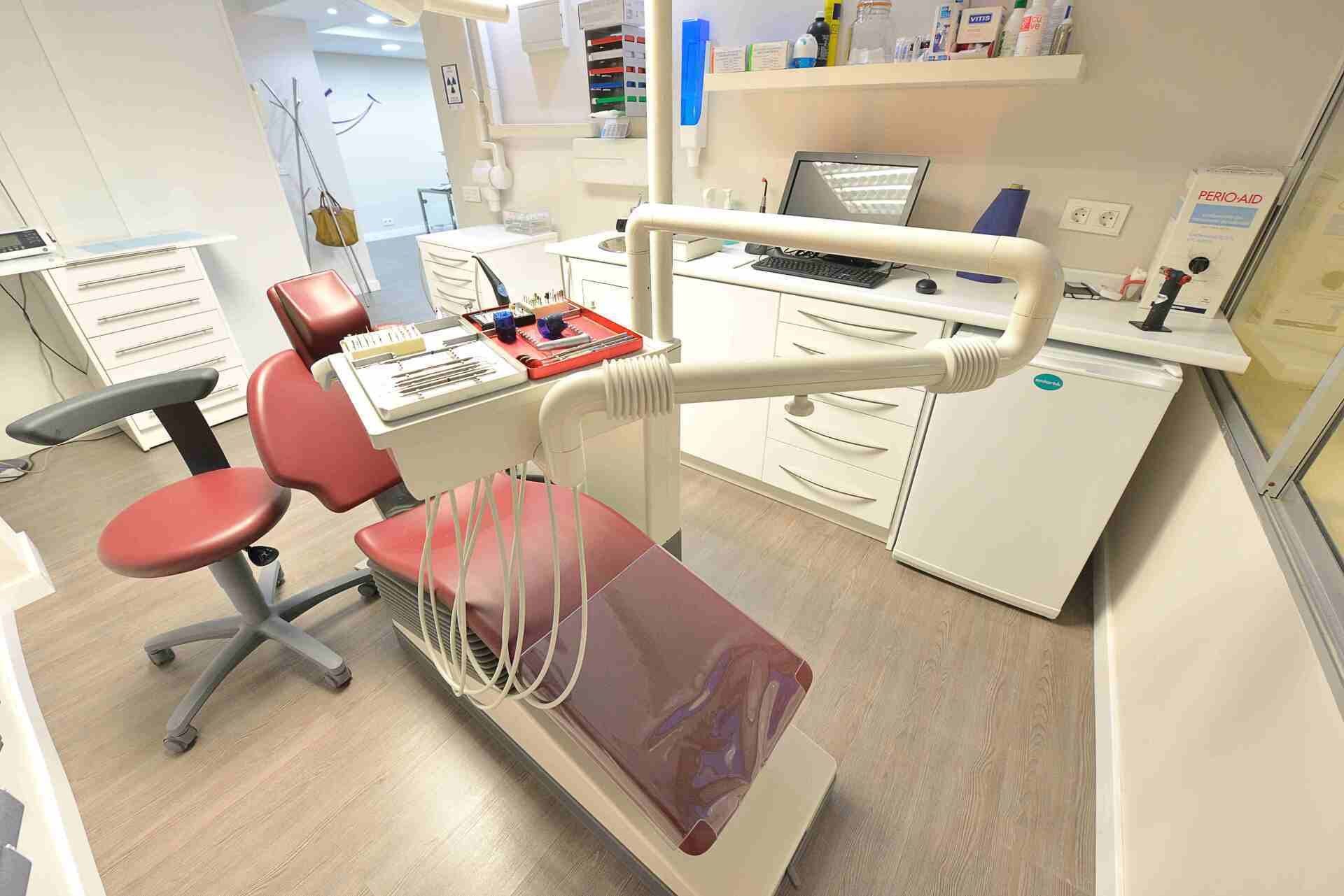 Un consultorio dental con un sillón dental rojo y un escritorio blanco.
