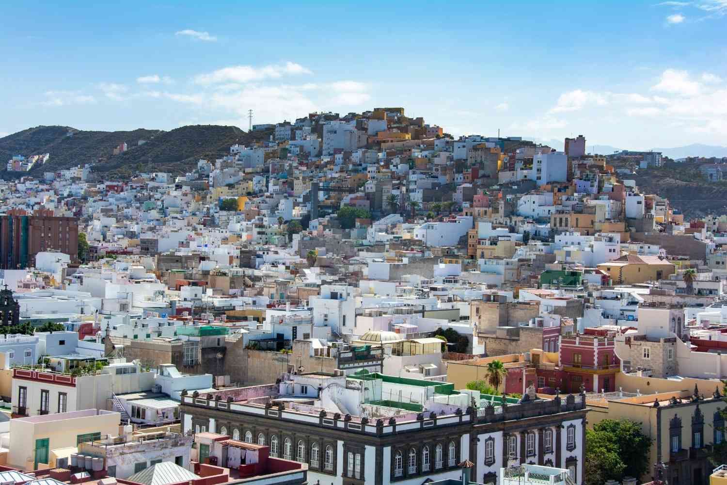 Paisaje urbano denso en la ladera de una colina con edificios blancos y una montaña al fondo.