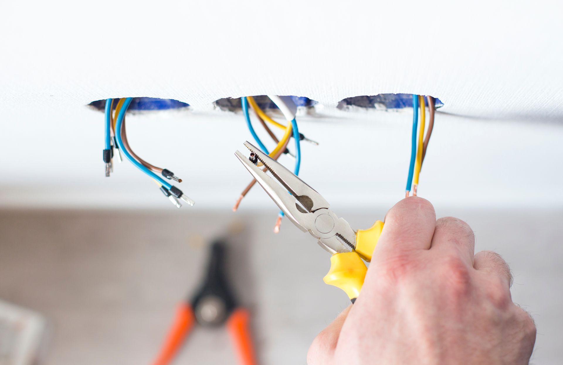 Un électricien dénude les fils d'une boîte de jonction au plafond à l'aide d'une pince.