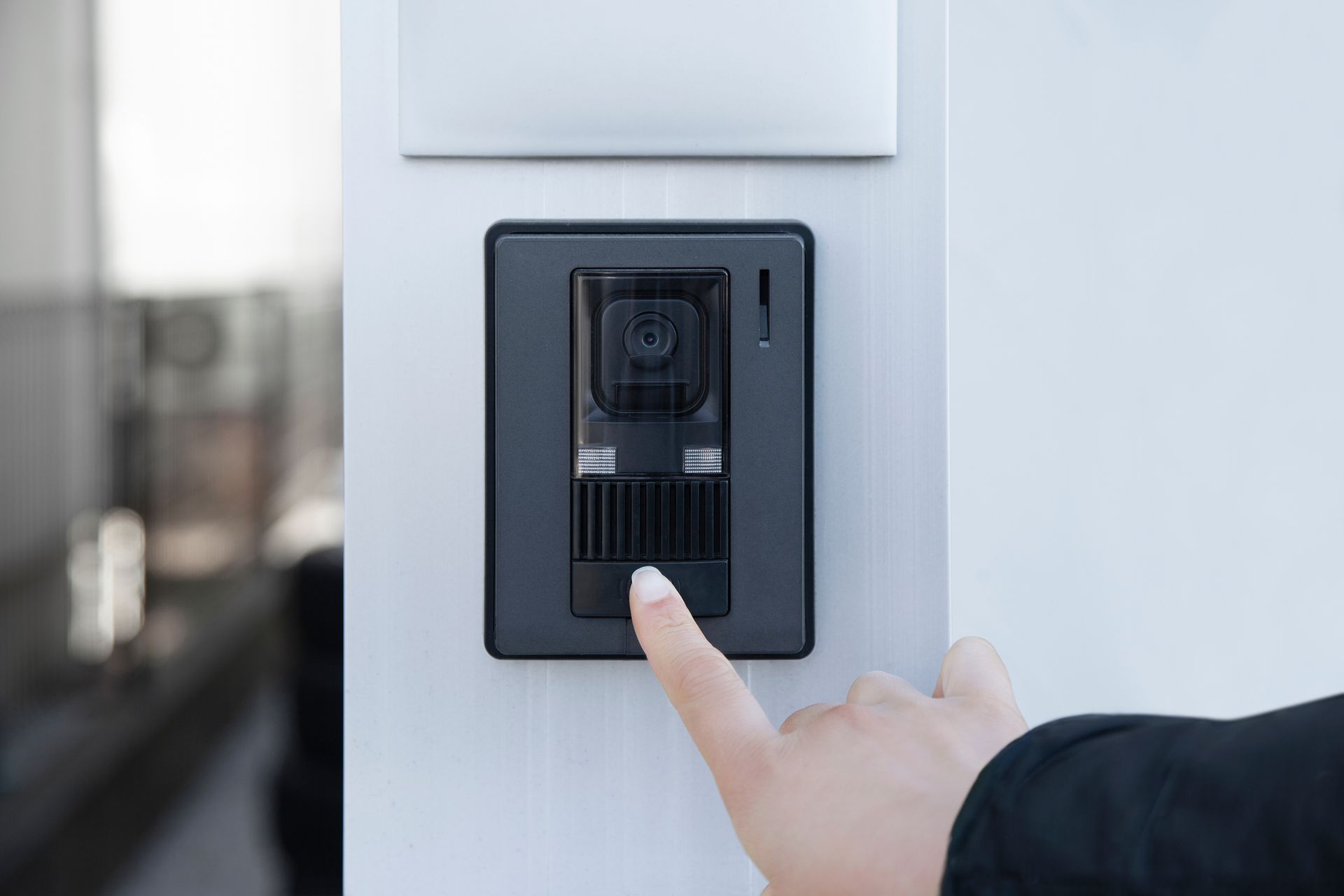 Le doigt d'une personne appuyant sur le bouton d'un interphone de porte moderne, de couleur, avec caméra intégrée.