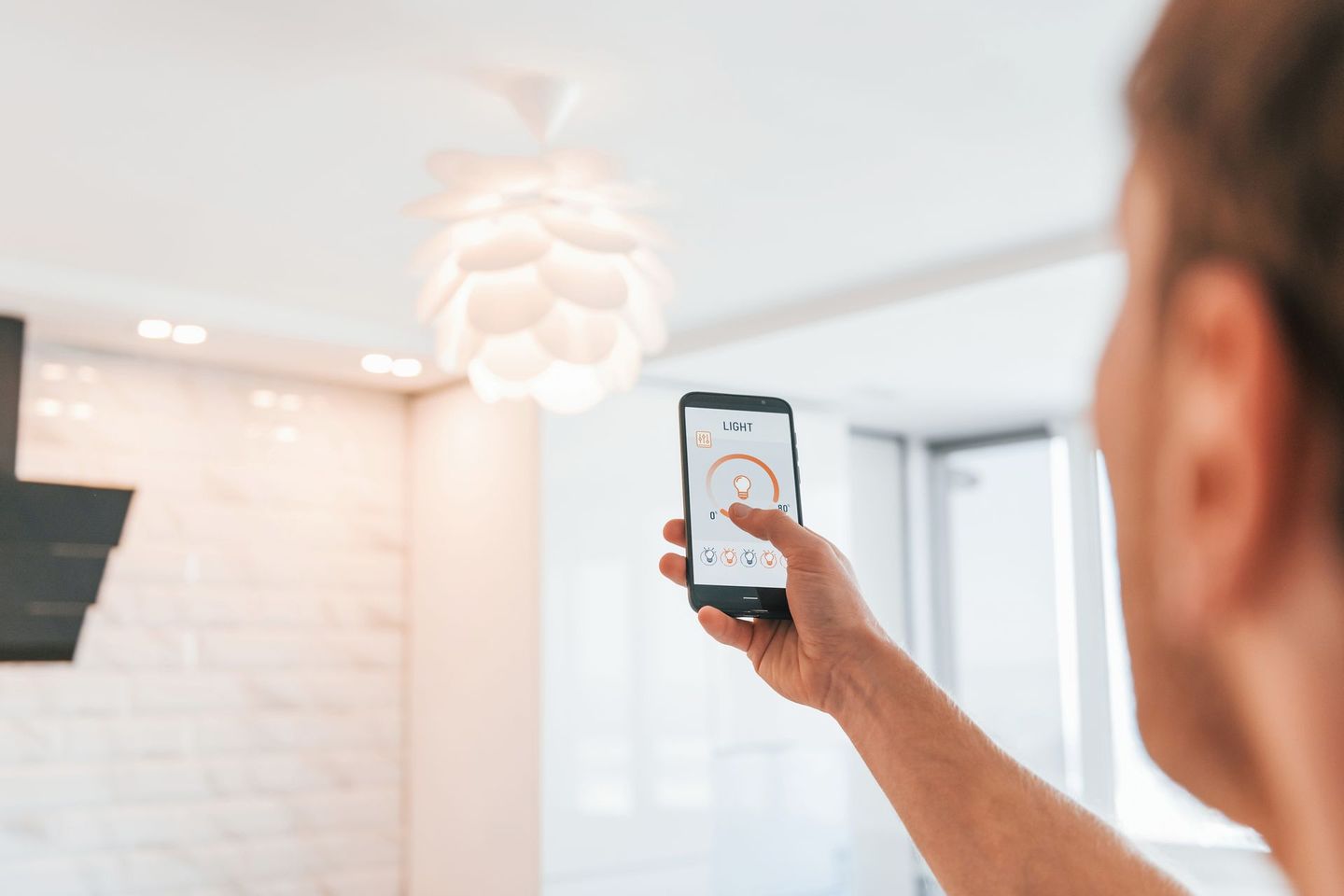Une personne utilise une application pour smartphone afin de régler un plafonnier moderne dans une pièce contemporaine.