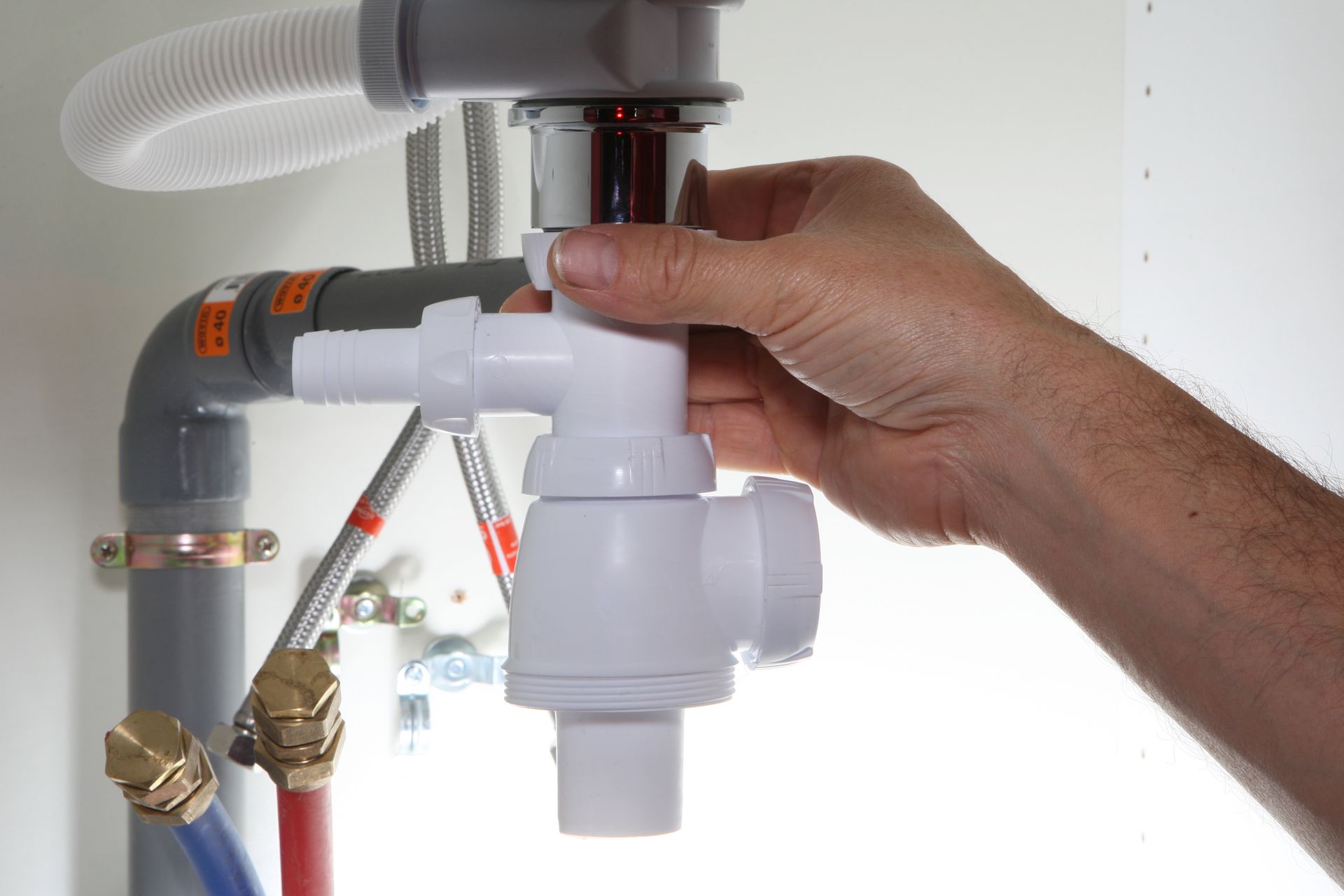 Une personne raccorde un siphon de plomberie en plastique à un tuyau d'évacuation d'évier sous un meuble.