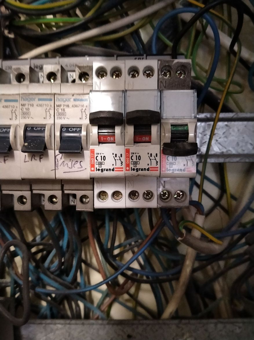 Gros plan sur un tableau de distribution électrique encombré, comportant plusieurs disjoncteurs, dont l'un est éteint.
