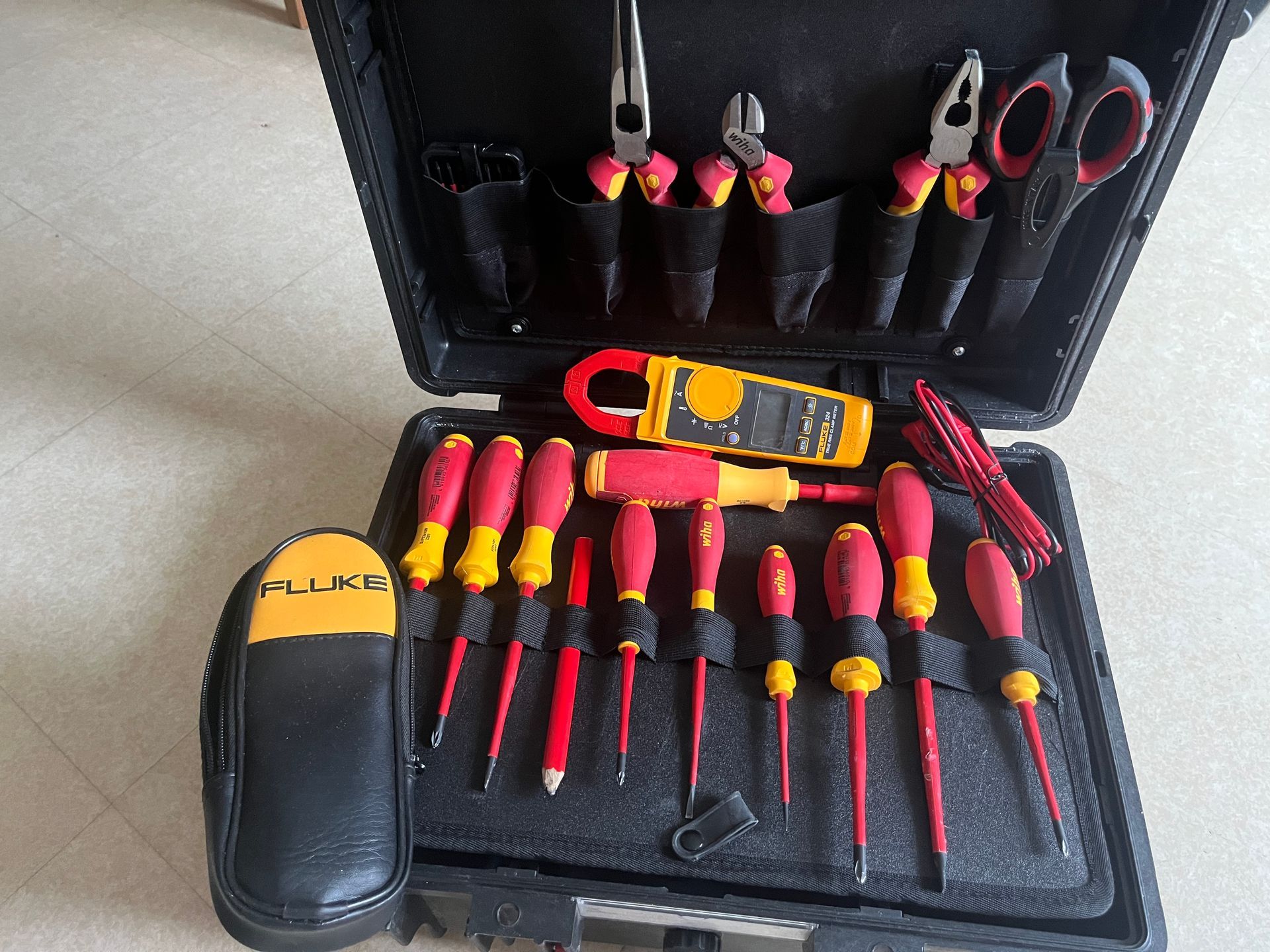 Une trousse à outils d'électricien professionnel dans un étui rigide ouvert, comprenant des outils isolés et un multimètre Fluke.