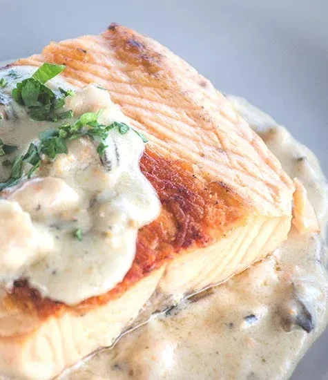 Filete de salmón a la sartén con salsa cremosa de champiñones, adornado con hierbas.