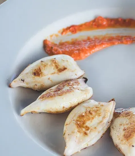 Calamares a la plancha en plato blanco con salsa roja.