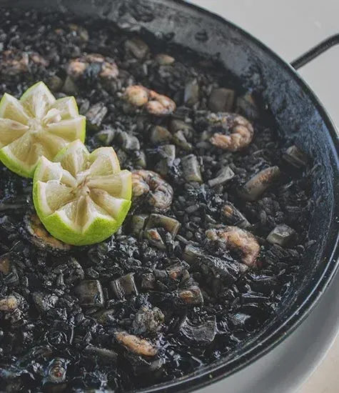Paella negra con marisco y gajos de lima en paellera negra.