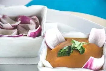 Dos platos cuadrados blancos: uno con rodajas de cebolla roja y el otro con salsa marrón adornada con cilantro.