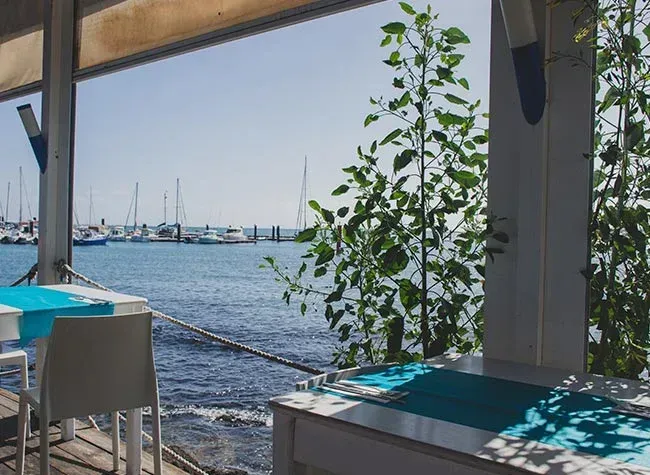 Vista desde un restaurante al aire libre con vistas a un puerto deportivo en un día soleado.