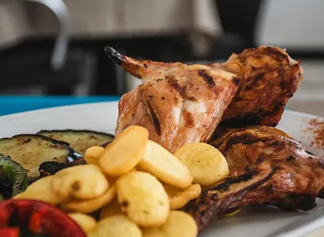 Pollo a la parrilla con patatas y verduras en un plato blanco.