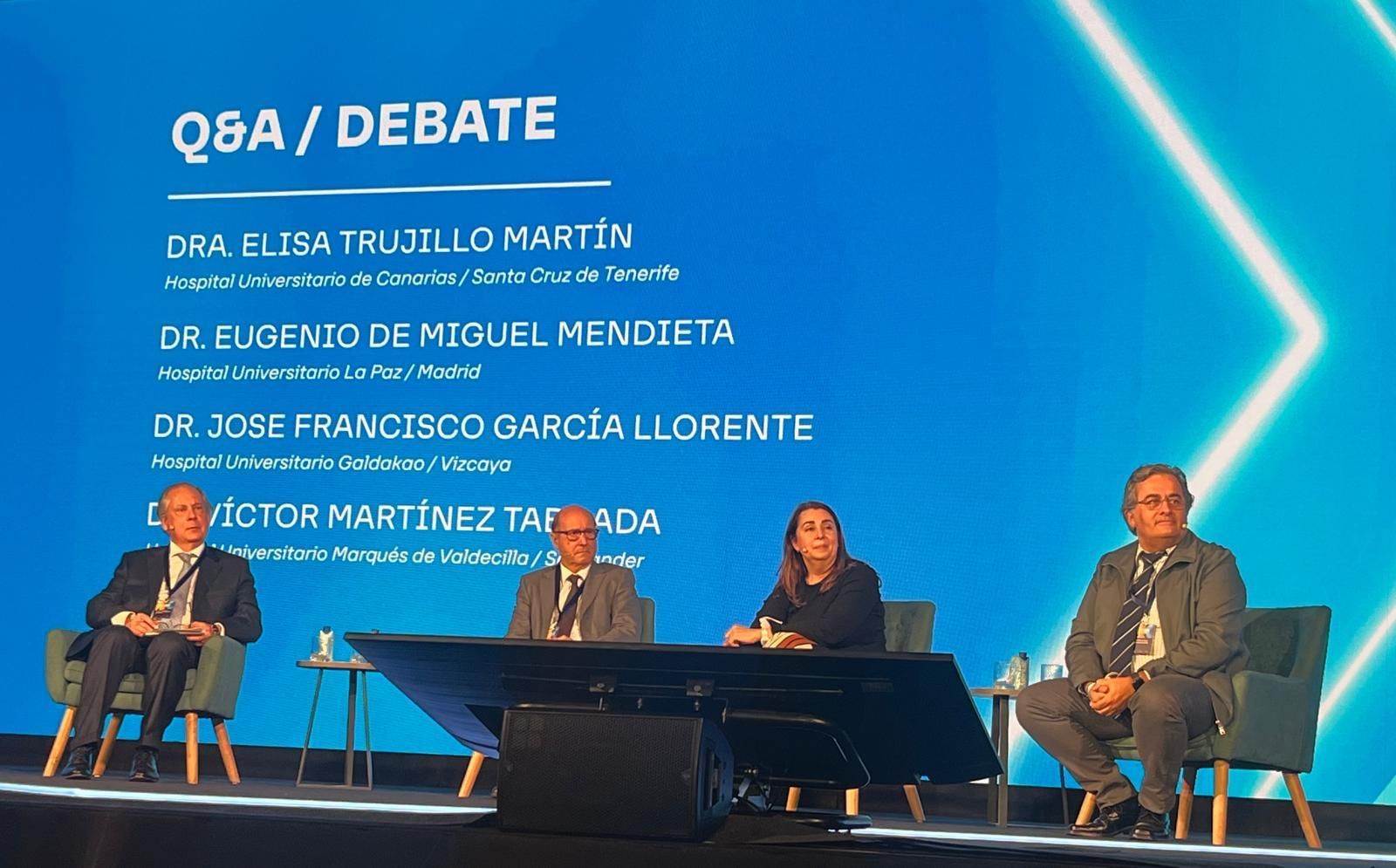 Un grupo de personas está sentado frente a una pantalla que dice q8a / debate