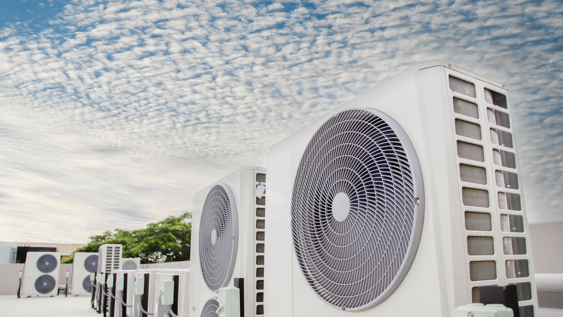 Des unités de climatisation blanches alignées sur un toit se détachant sur un ciel nuageux.