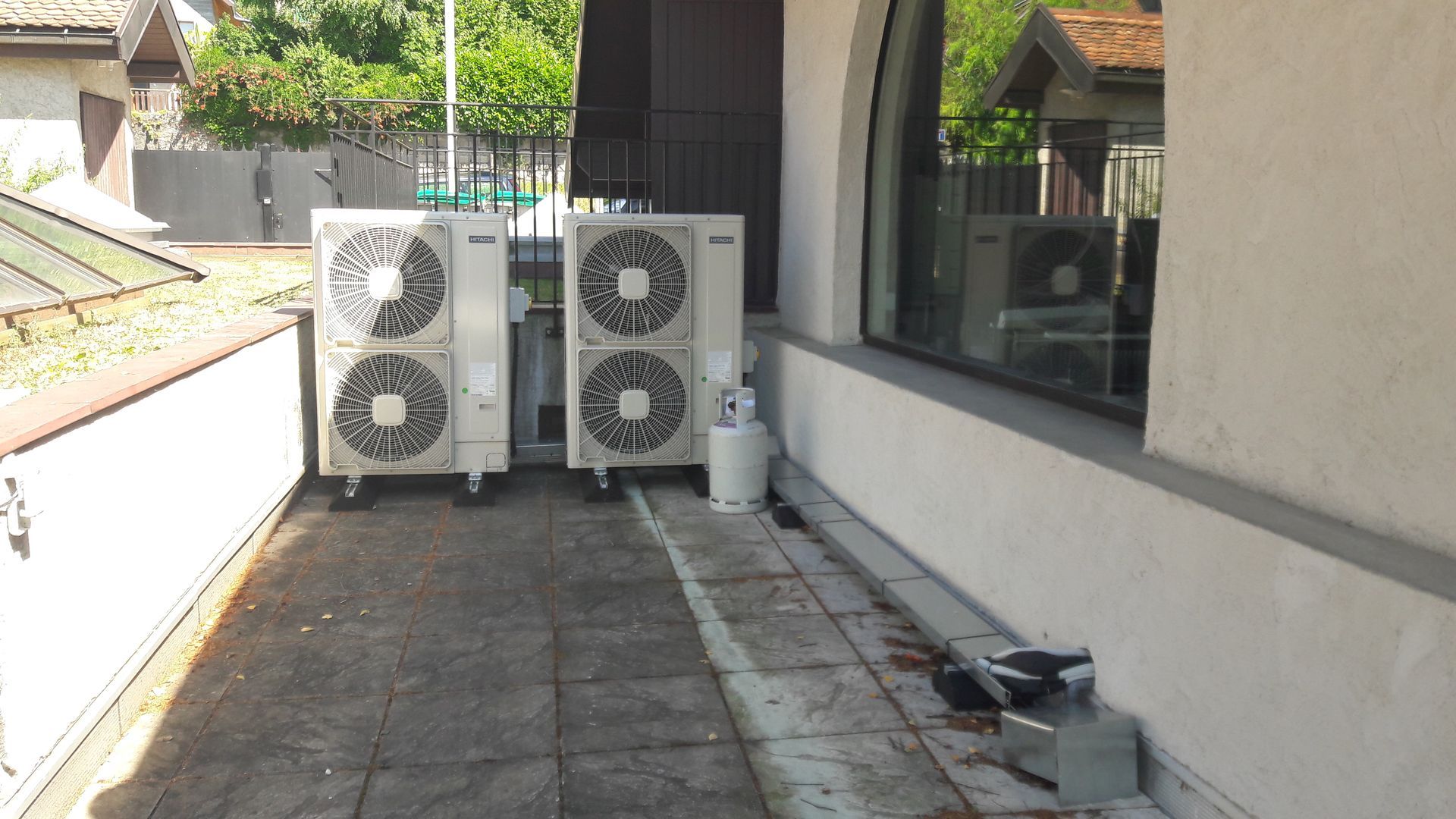 Deux unités de climatisation blanches sur une terrasse en béton près d'un bâtiment doté d'une grande fenêtre.