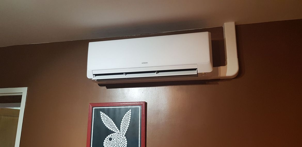Unité de climatisation blanche fixée sur un mur marron, avec une photo encadrée en noir et blanc d'un lapin en dessous.