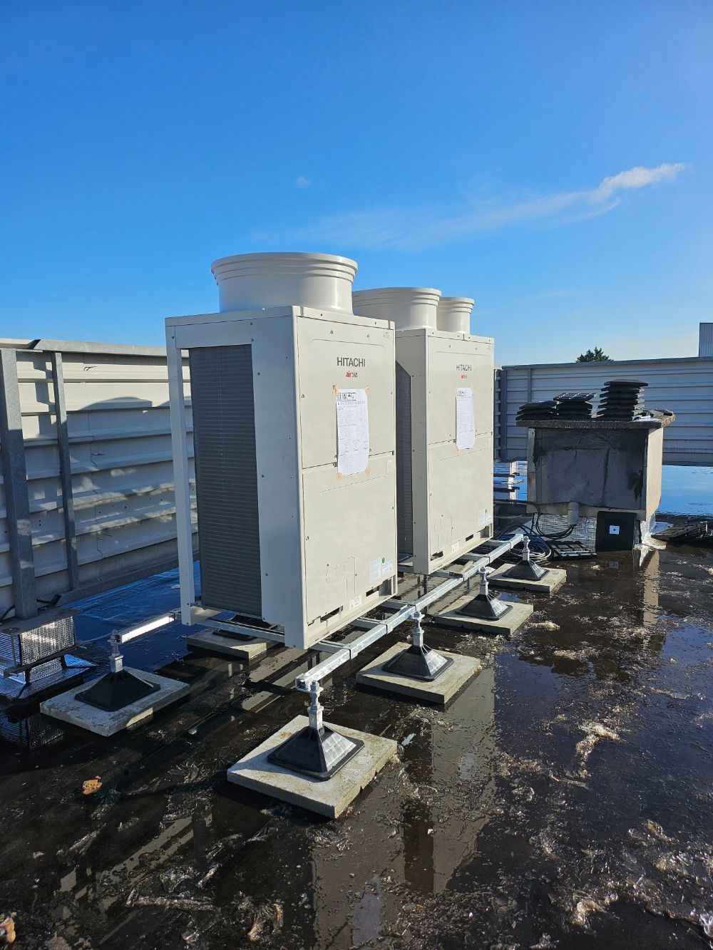 Unité de climatisation fixée sur un mur extérieur couleur pêche, à côté d'une porte blanche. Ciel couvert.
