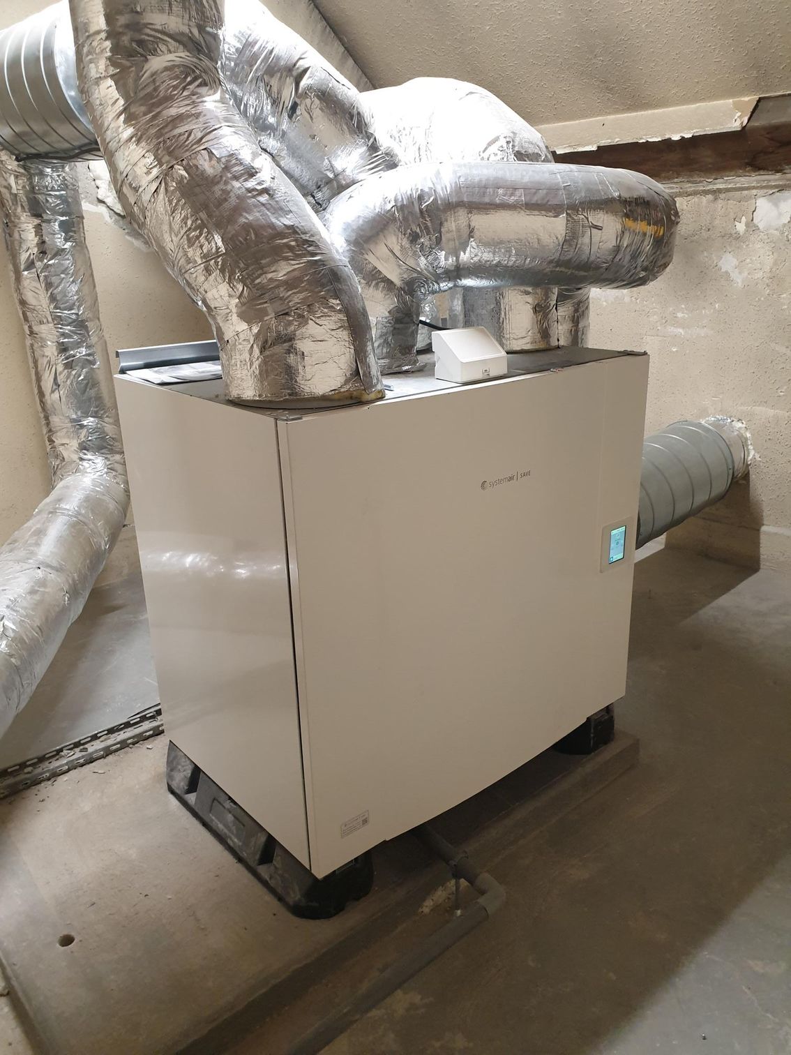 Unité de ventilation blanche avec conduits argentés dans un sous-sol.