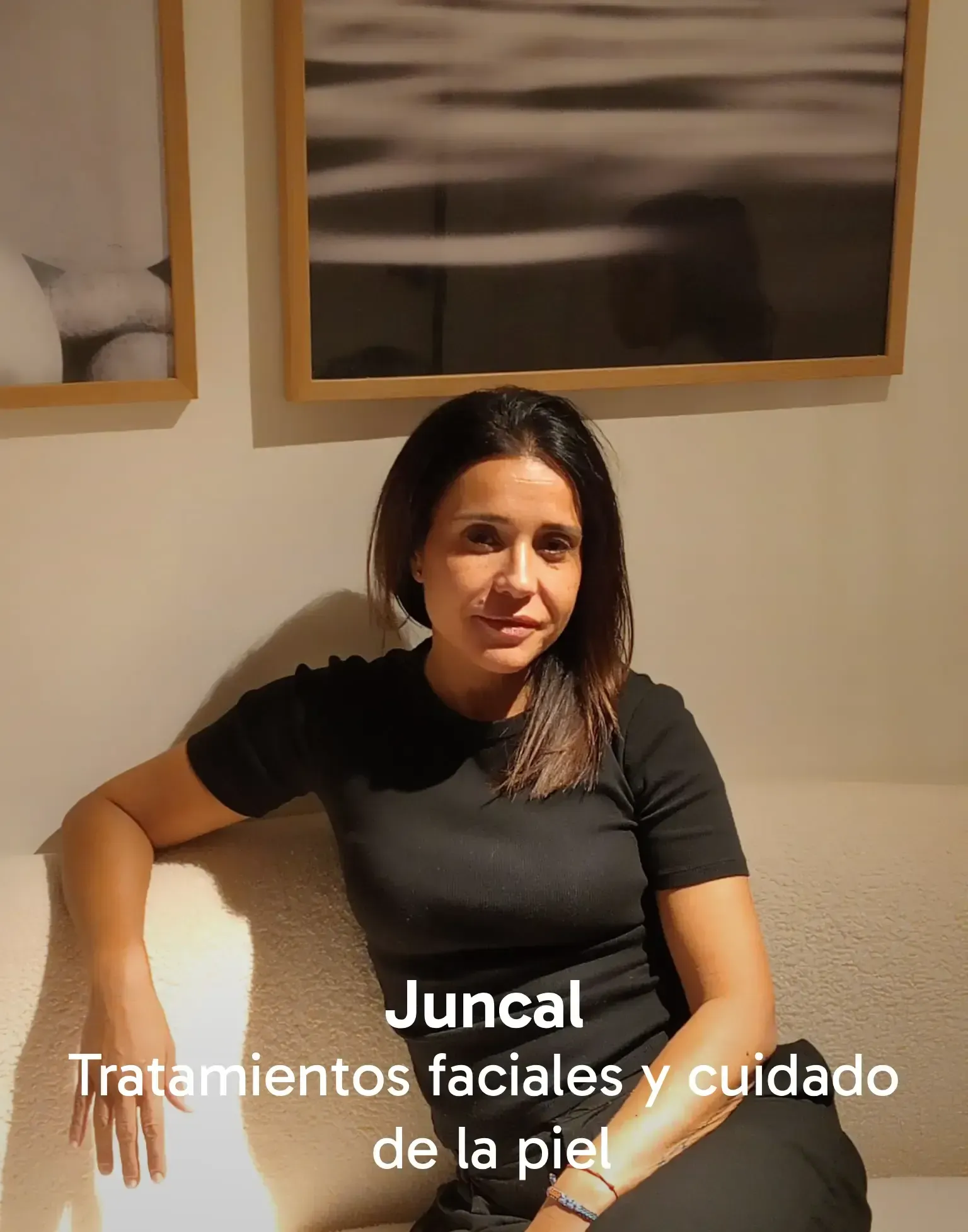 María Miquel Casares, psicóloga, está sentada sonriendo en un sofá color crema en una habitación con obras de arte.