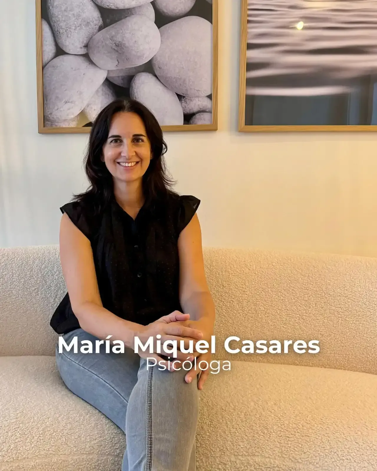 María Miquel Casares, psicóloga, está sentada sonriendo en un sofá color crema en una habitación con obras de arte.