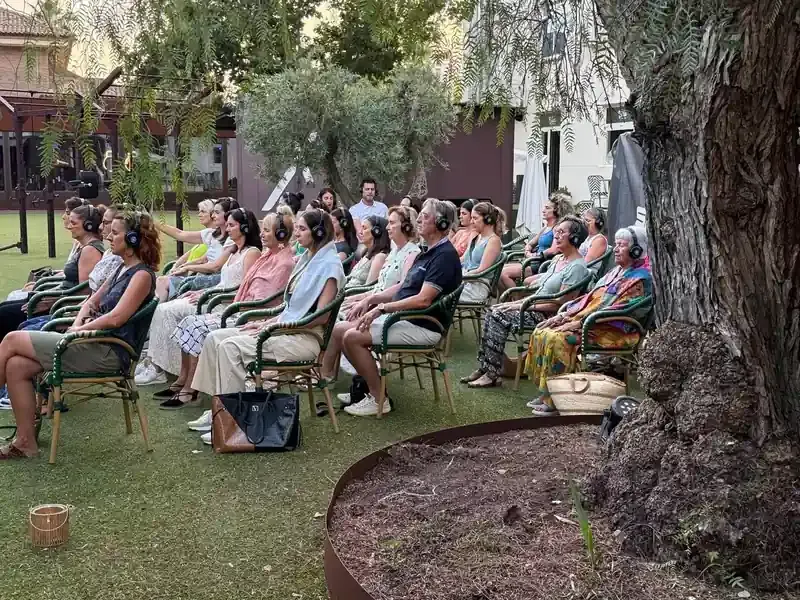 Personas con auriculares sentadas al aire libre, escuchando; un entorno de jardín.