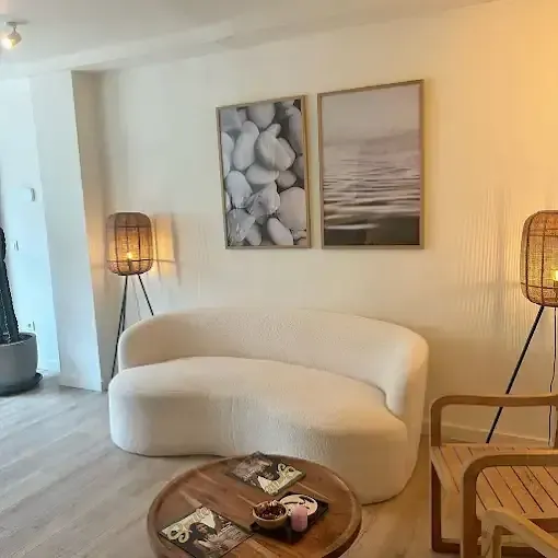 Acogedora sala de estar con sofá color crema, mesa de centro redonda, cuadros enmarcados y lámparas de ratán.