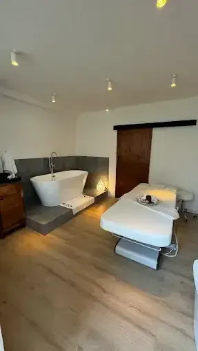 Habitación de spa con bañera, camilla de masaje y puerta corredera de madera.