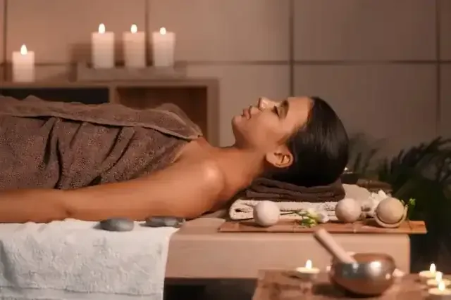 Mujer relajándose en una camilla de masaje, en un ambiente de spa con velas y piedras.