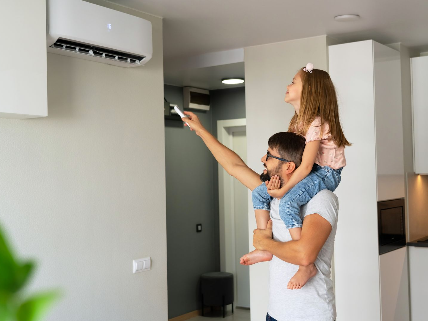 Dans une maison, une personne tenant la télécommande du climatiseur avec un enfant sur les épaules.