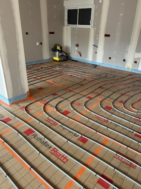 Tuyaux installés sur une dalle pour chauffage au sol avec un collecteur dans le mur.