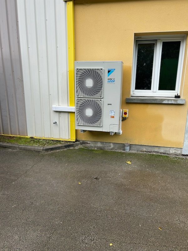 Unité de climatisation extérieure  avec deux ventilateurs près d'un bâtiment.