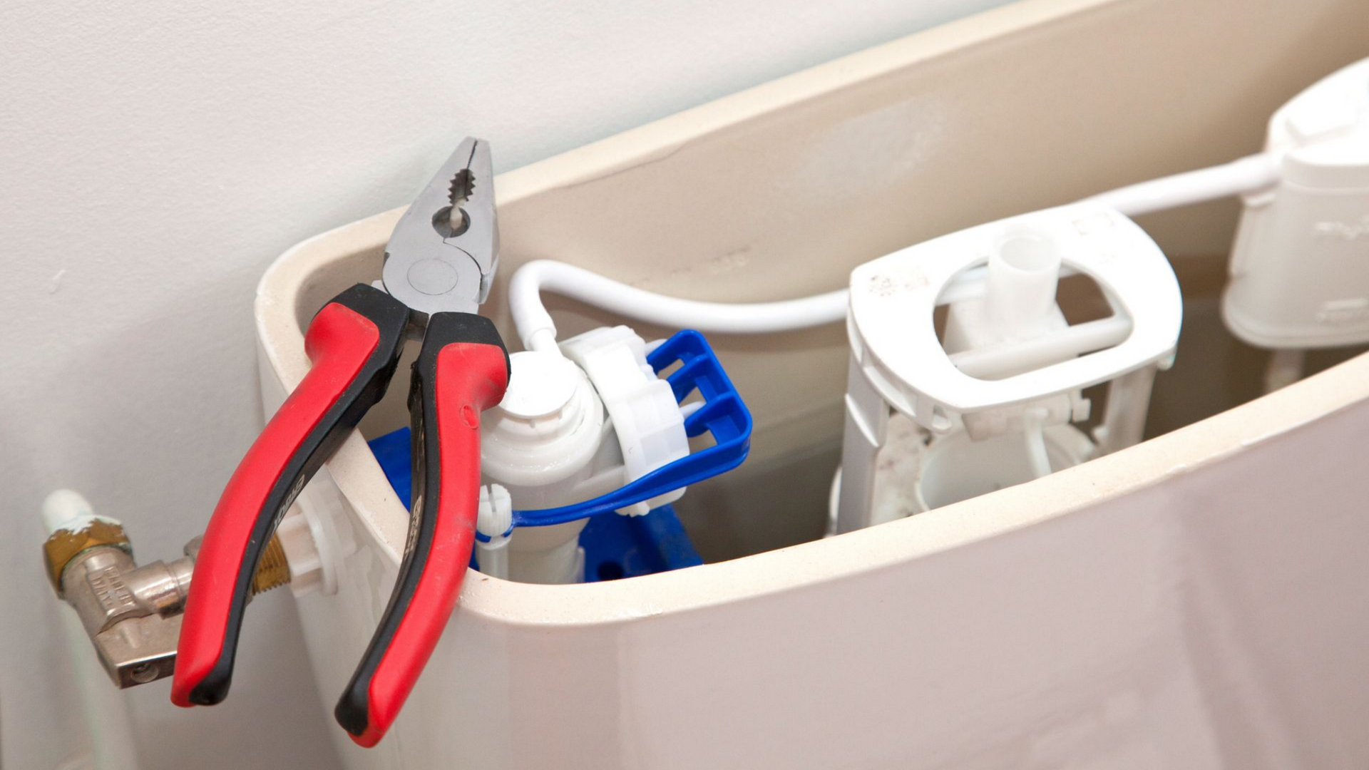 Une pince coupante posée sur le réservoir des toilettes. Elle se trouve à côté du robinet de remplissage et du flotteur.