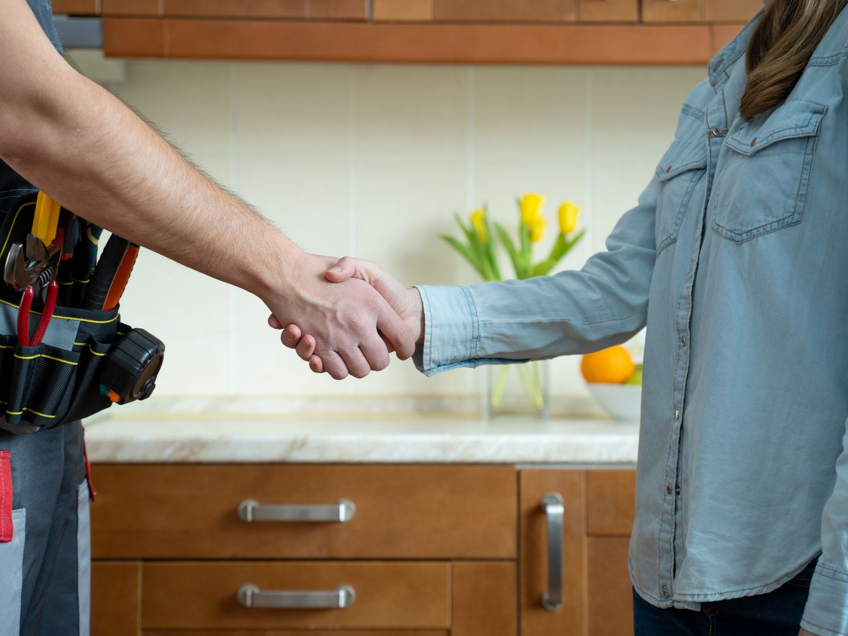 Dans une cuisine, une personne en chemise en jean serre la main d'une autre portant une ceinture à outils.
