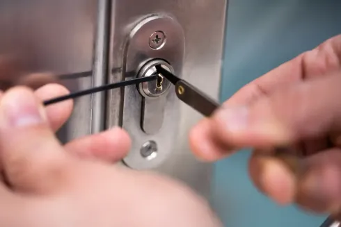 Manos utilizando una ganzúa en un cilindro de cerradura de puerta plateado